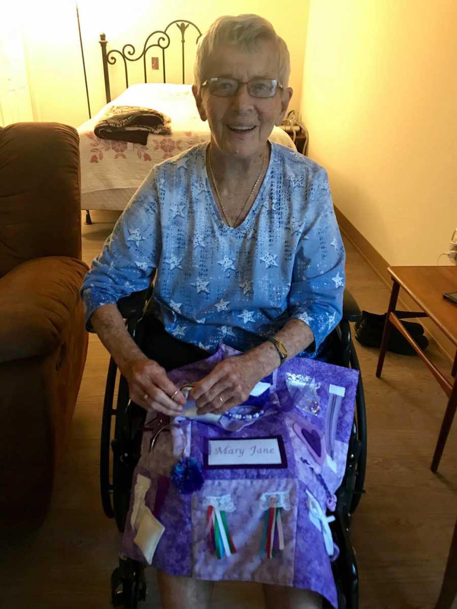 Elderly woman with dementia sits smiling in wheelchair in her nursing home bedroom