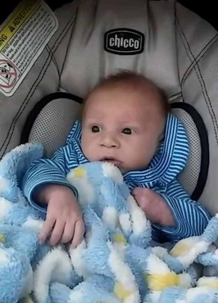 Baby sits in car seat in blue and white stripe shirt with blue blanket