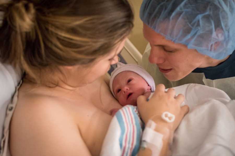 Mother looking down at newborn with Trisomy 18 lying on her while husband stands over newborn