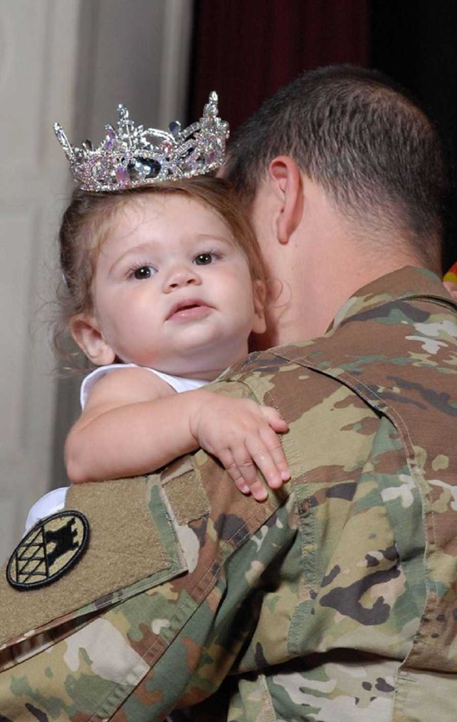 infant with crown on hugs father who is holding her in his uniform