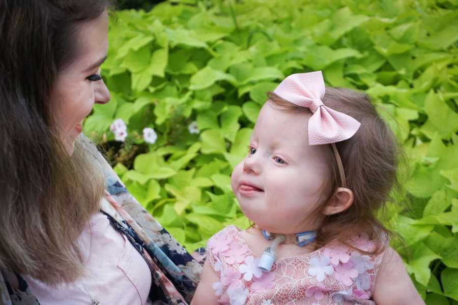 Mother smiling at daughter with Trisomy 18 that is sitting in her lap 