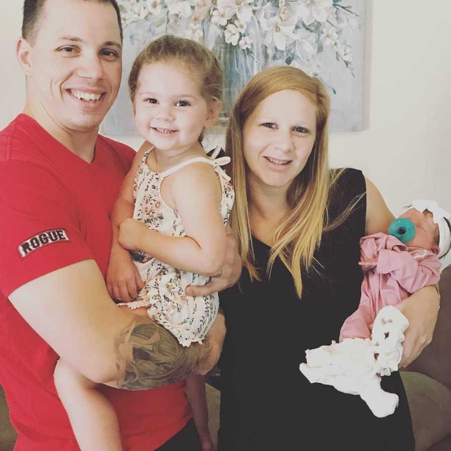 Soldier husband holds first born smiling beside wife who holds newborn