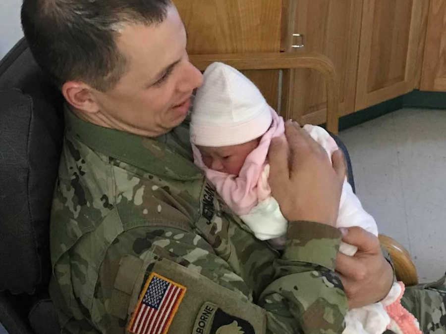 Soldier sits in uniform in hospital room holding newborn daughter