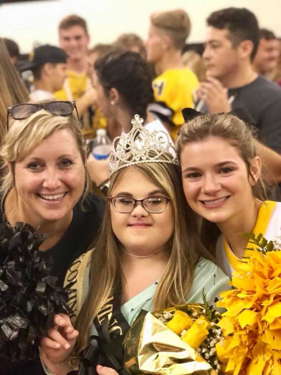 Teacher smiles beside down syndrome homecoming queen and cheerleader