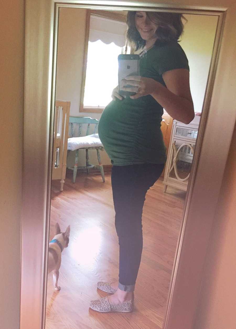 Pregnant woman smiles in mirror selfie while holding her stomach in nursery