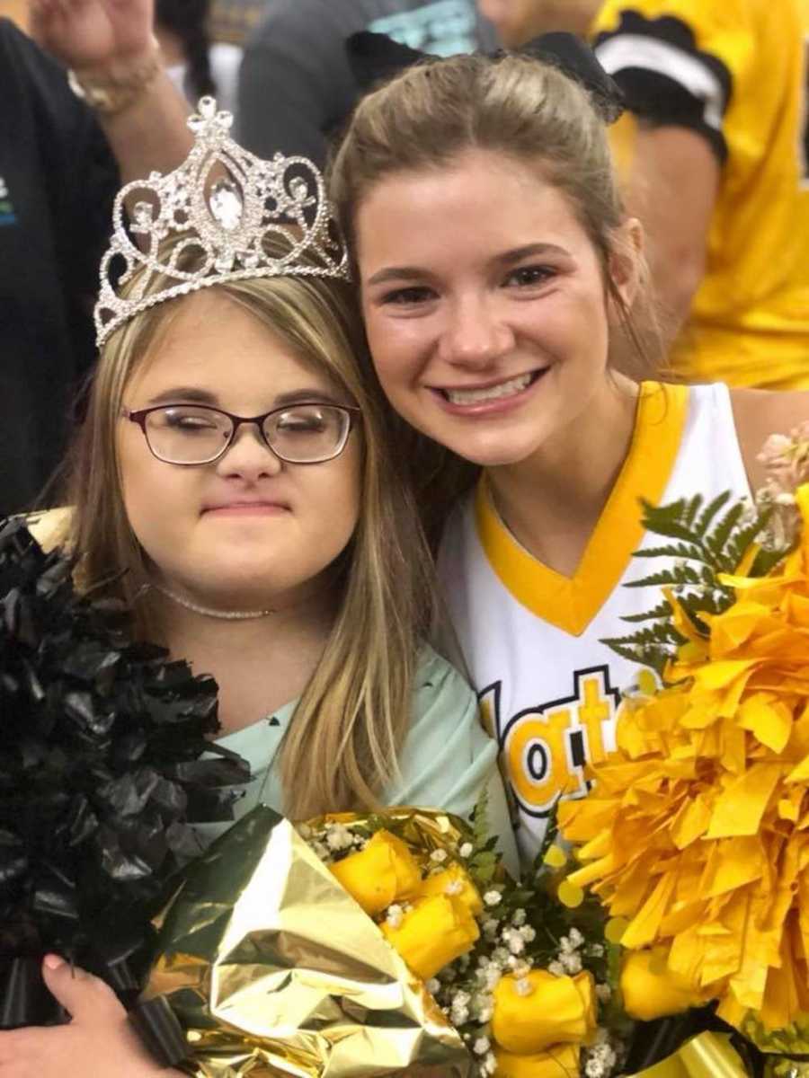 High school cheerleader smiles beside teen with down syndrome with crown on