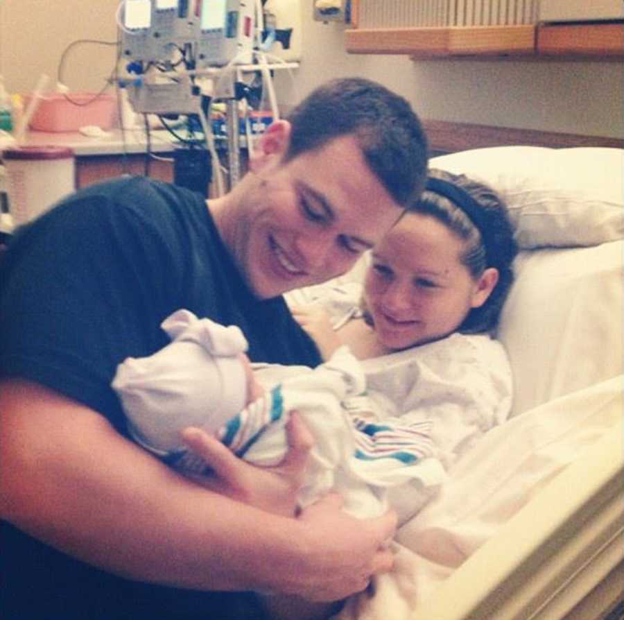 Woman who just gave birth smiles at newborn that is in her husband arms beside her