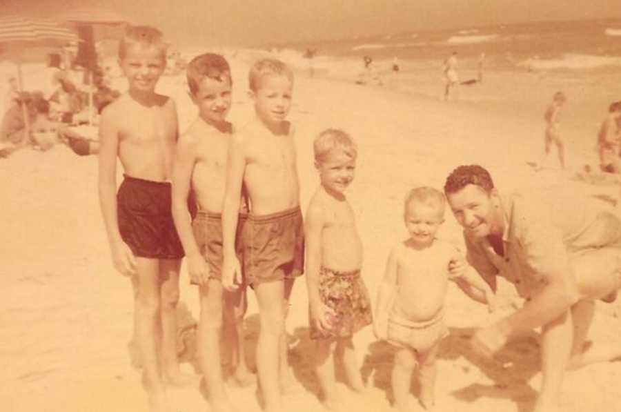Father squatting beside youngest son on beach with four other sons standing beside him