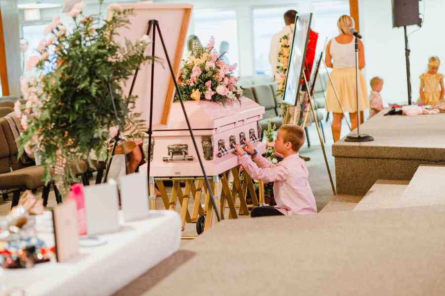 Little boy sits in front of coffin resting his hands on it 