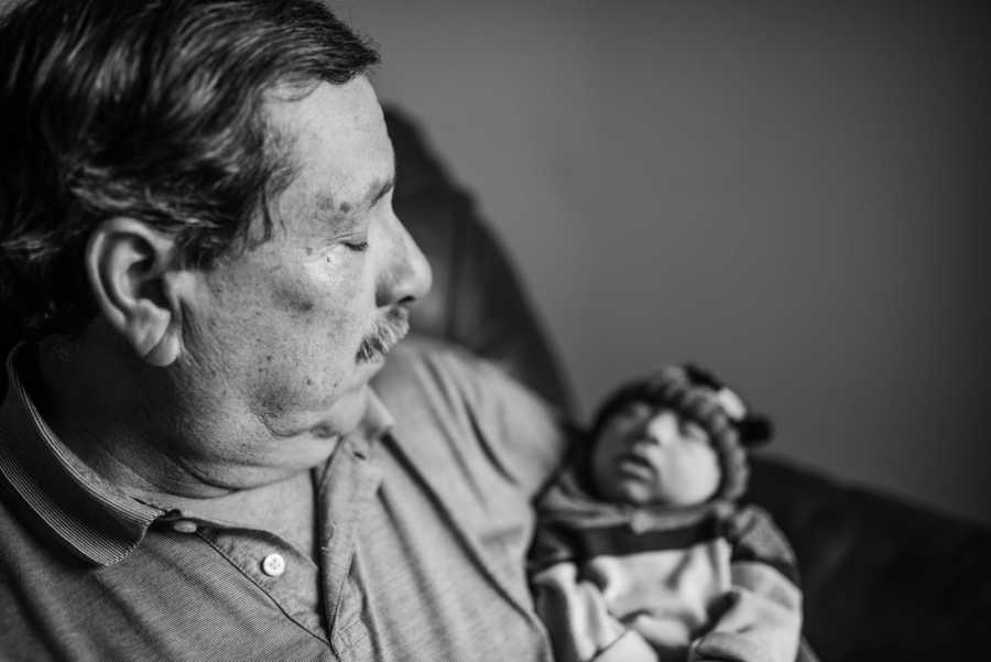 Grandfather looks down at baby with Microcephaly sleeping in his arms