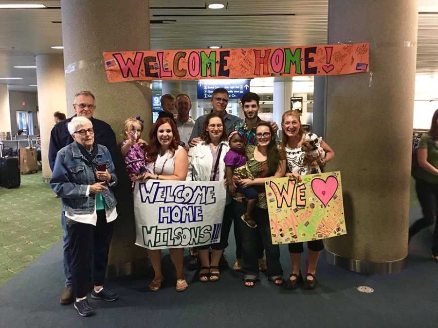 Woman and her adopted daughter from Ghana are greeted by family at airport with welcome home signs