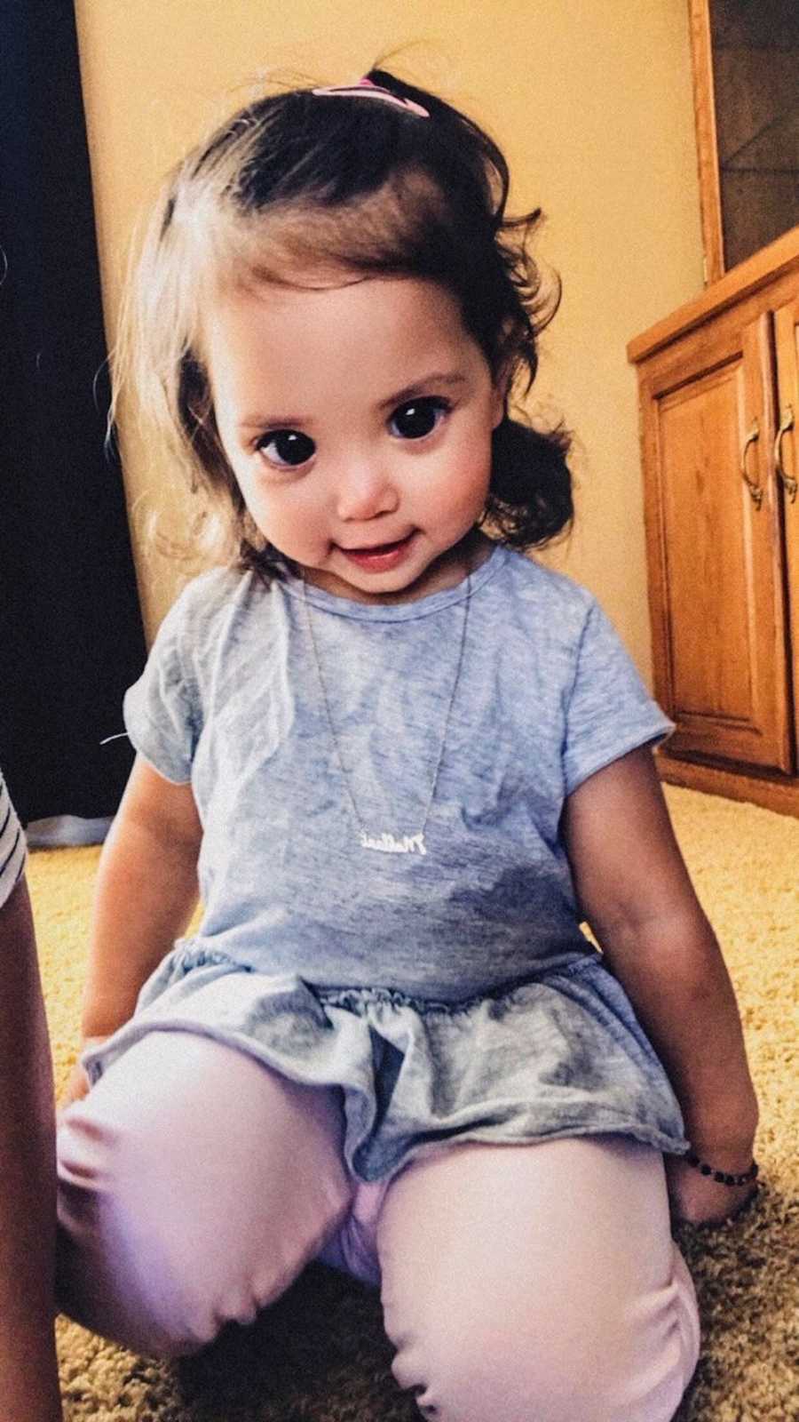 Toddler with Axenfeld-Rieger syndrome whose eyes are mostly pupil, sits on her knees smiling