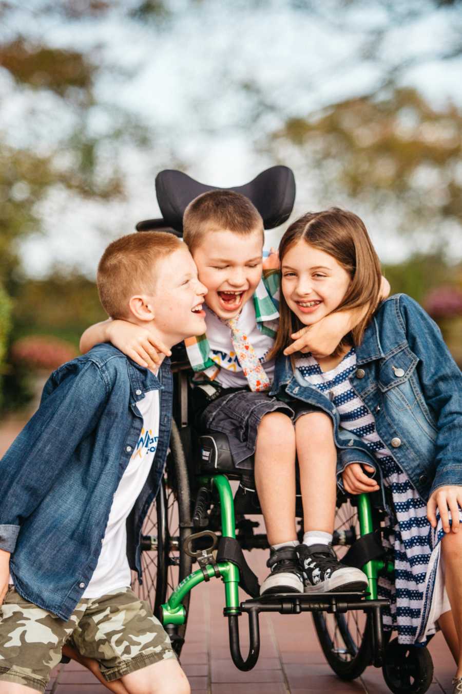 Young boy with vanishing white matter disease sits in wheelchair with arms around brother and sister