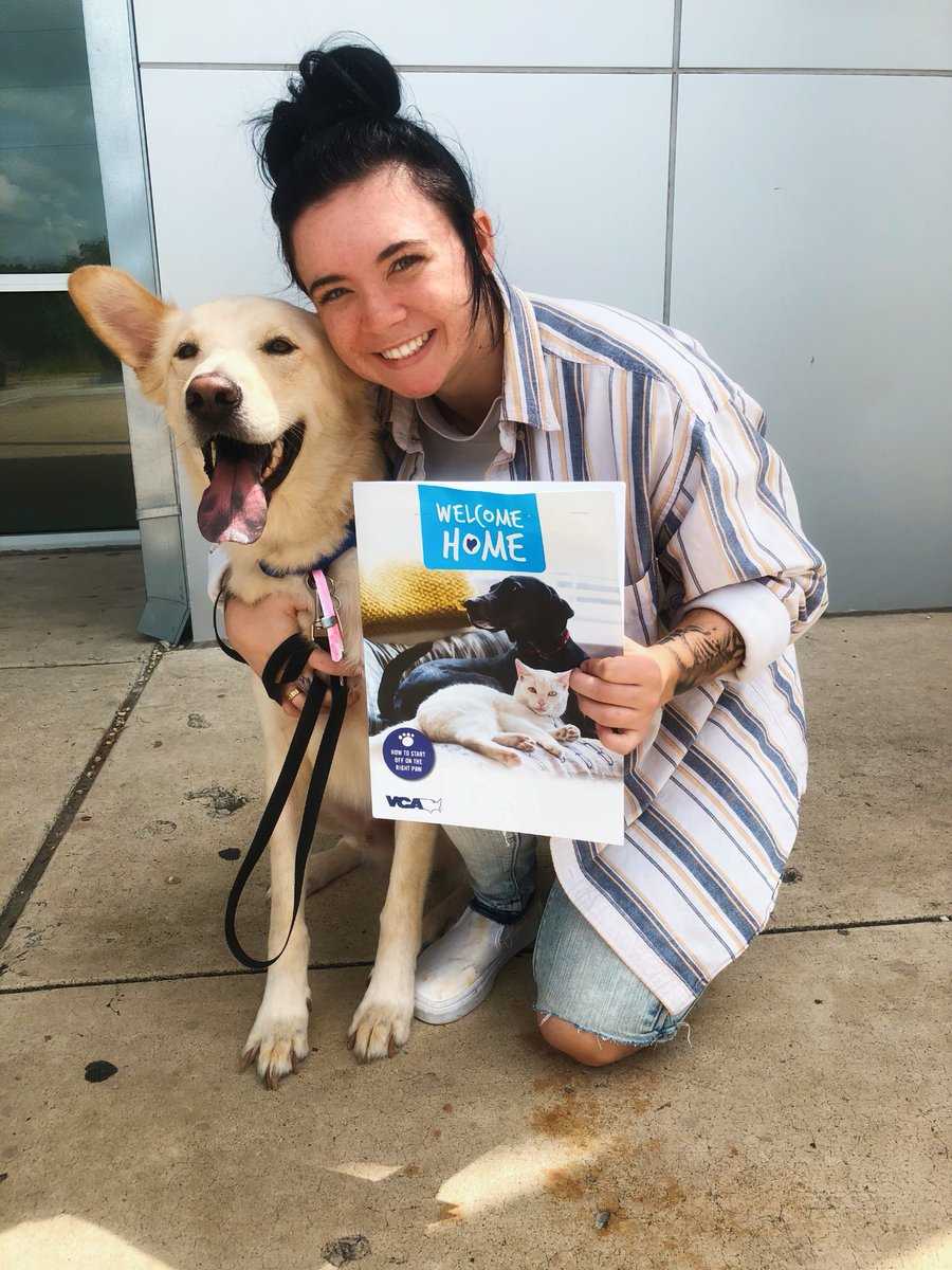 Young woman squats down smiling with her arm around adopted dog