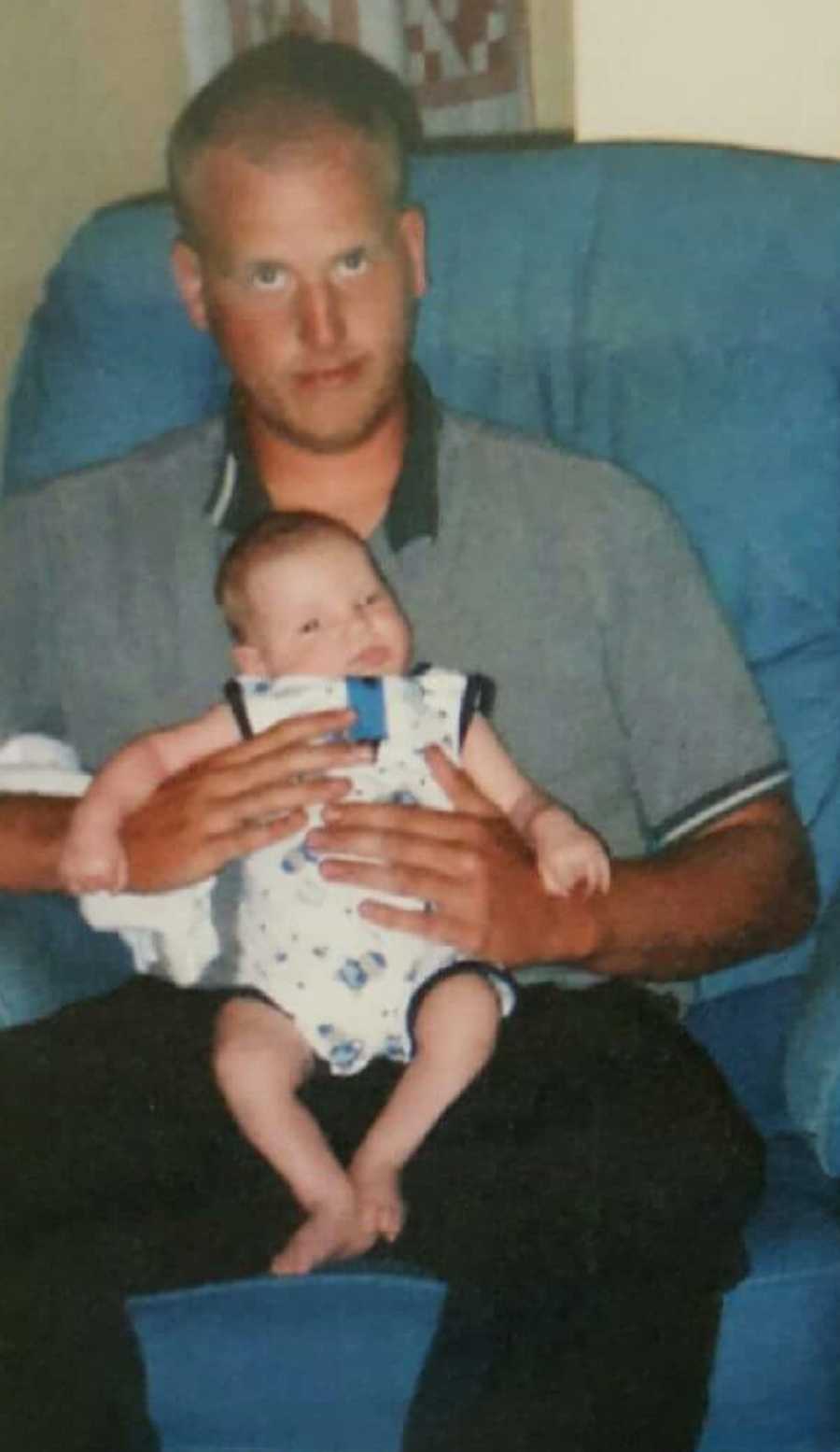 Man who was taken from parents as child sits in chair holding his newborn son