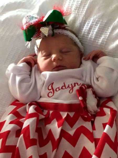 Newborn baby in red and white chevron dress and red, white, and green bow in her hair