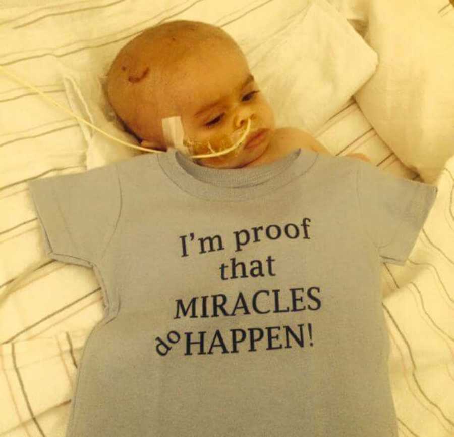 Baby lying in hospital bed with shirt over him that says, "I'm proof that miracles do happen"