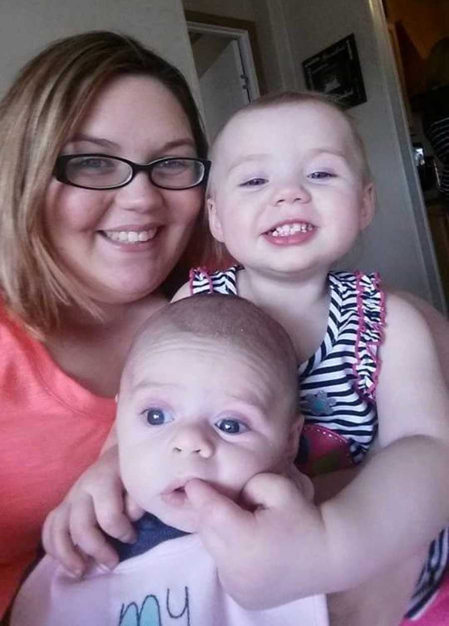 Mother in bad relationship smiles with toddler daughter and baby son
