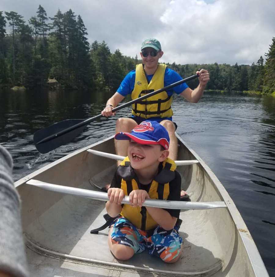 Boy with vanishing white matter disease sits smiling in canoe while father paddles behind him