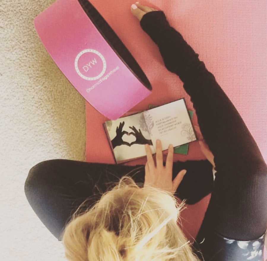 Aerial view of woman with fertility issues sits on yoga mat reading book 