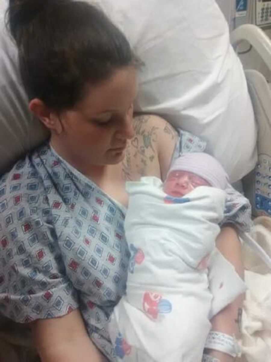 Woman who just gave birth sits in hospital bed looking down at newborn who won't make it