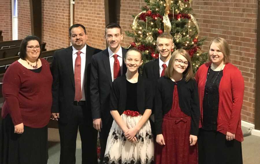 Foster parents stand beside foster children in church dressed for Christmas