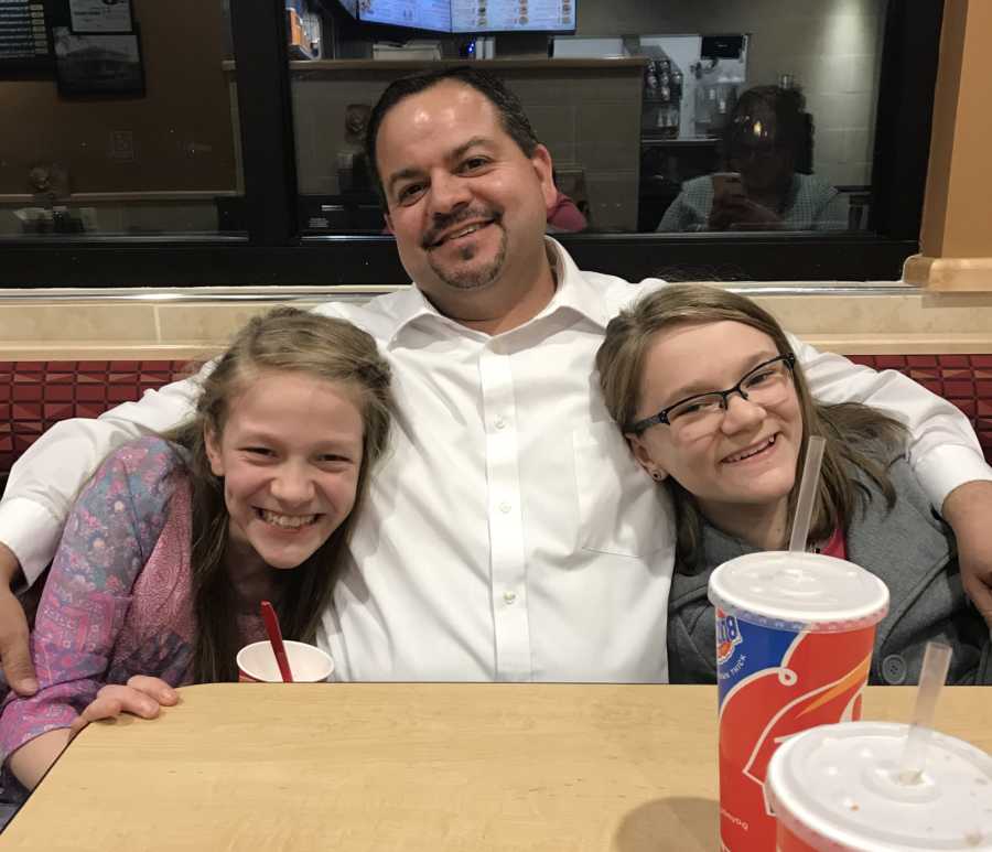 Foster father sits in booth of dairy queen with arms around two foster daughters