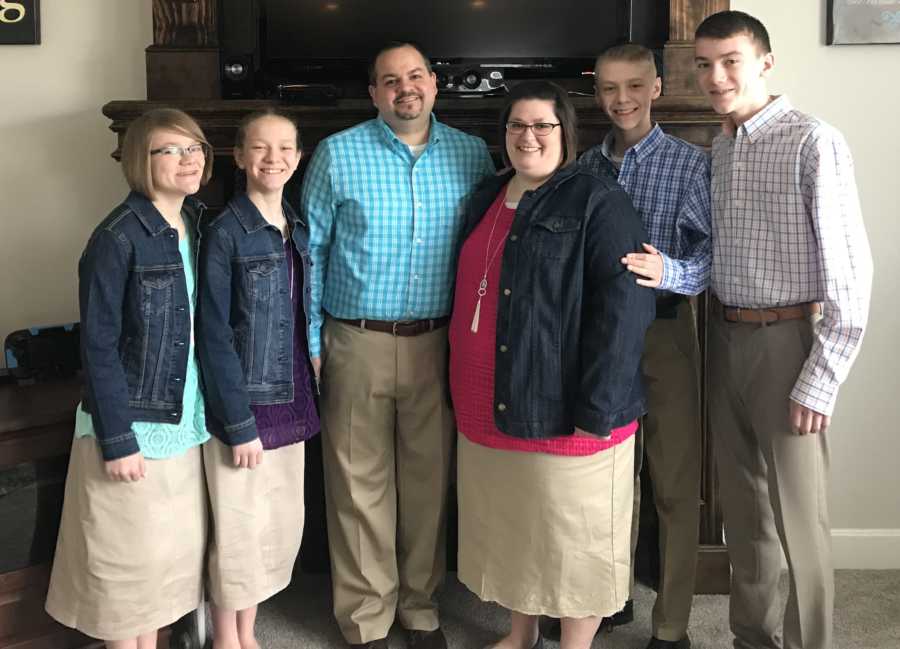 Husband and wife stand in front of fireplace smiling with four adopted children