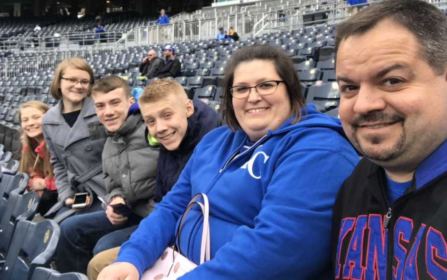 Foster father smiles in selfie at Kansas City Royals game beside wife and four foster kids