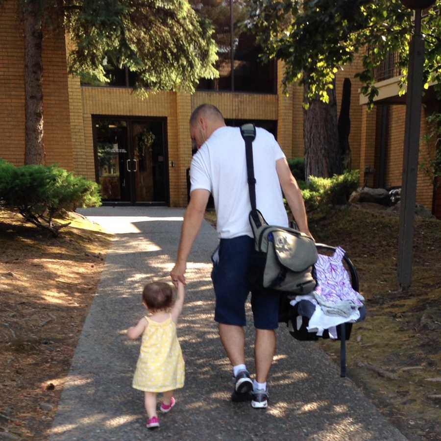 Grandfather holding grandchild's hand while holding carseat on other walking into building before he passed