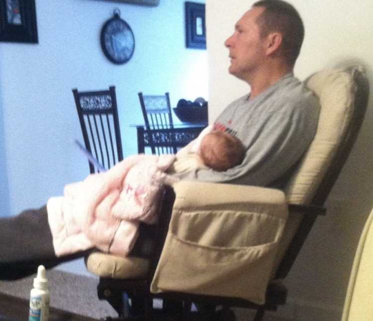 Father who was in delivery room with daughter sits in rocking chair holding granddaughter