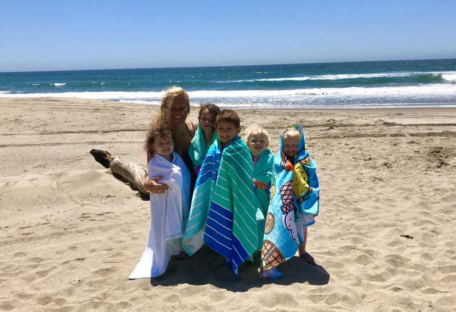 Mother kneels on beach beside her five kids whose school has grandparents day