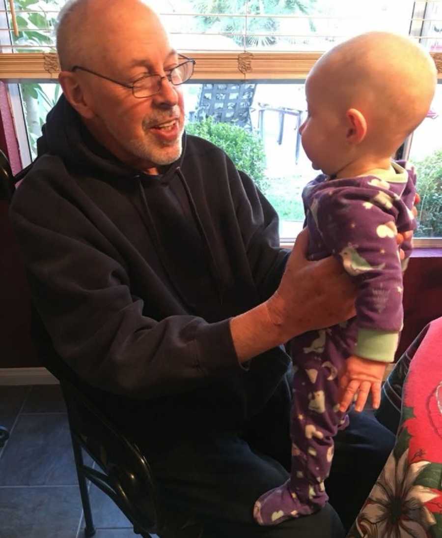 Man with cancer smiles as he sits holding up granddaughter