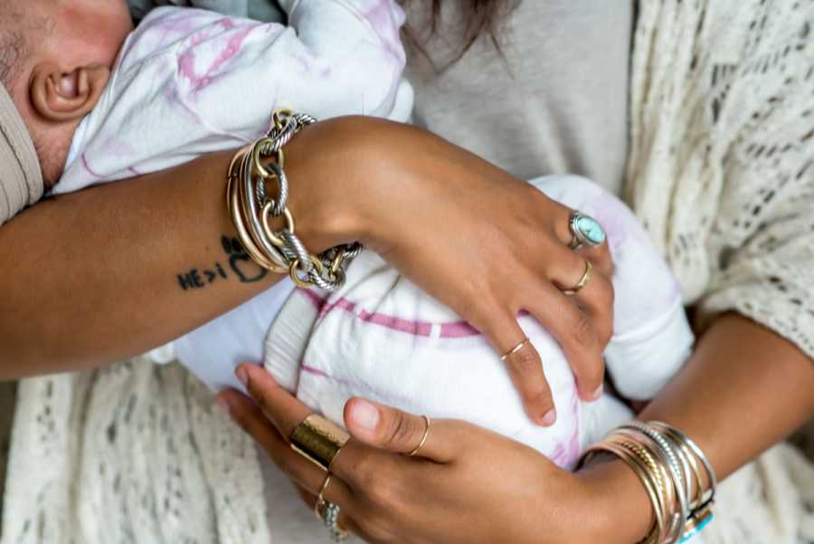 Close up of mother with lots of bracelets and rings on holding adopted newborn after several miscarriages