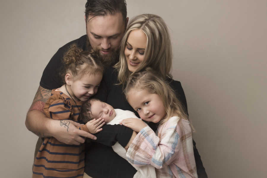 Mother holds newborn beside her two daughters and husband