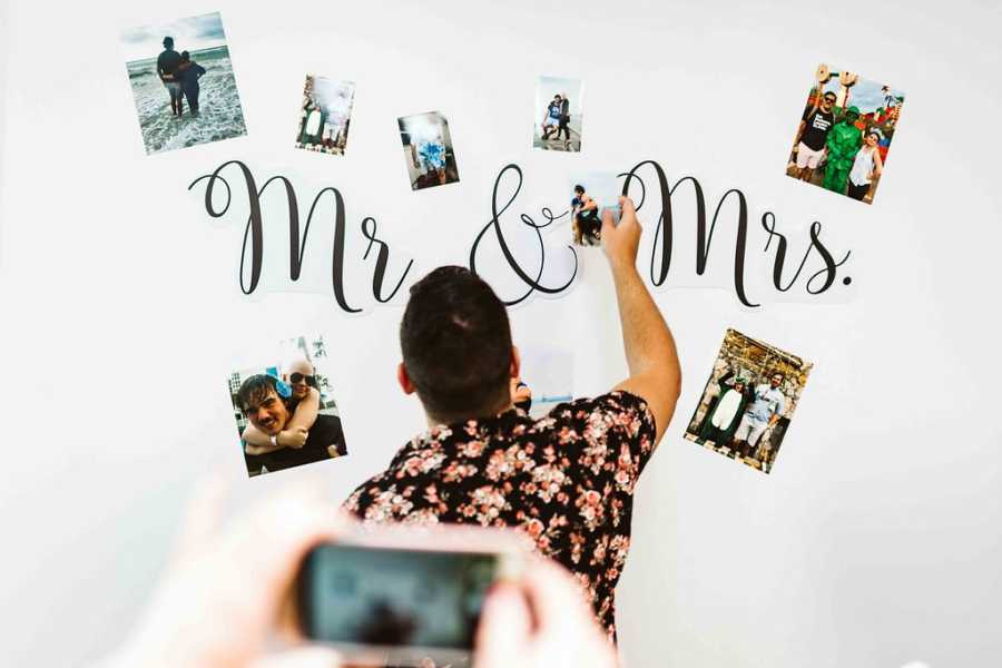 Man putting up picture on wall that says, "Mr & Mrs" with pictures of the couple around it