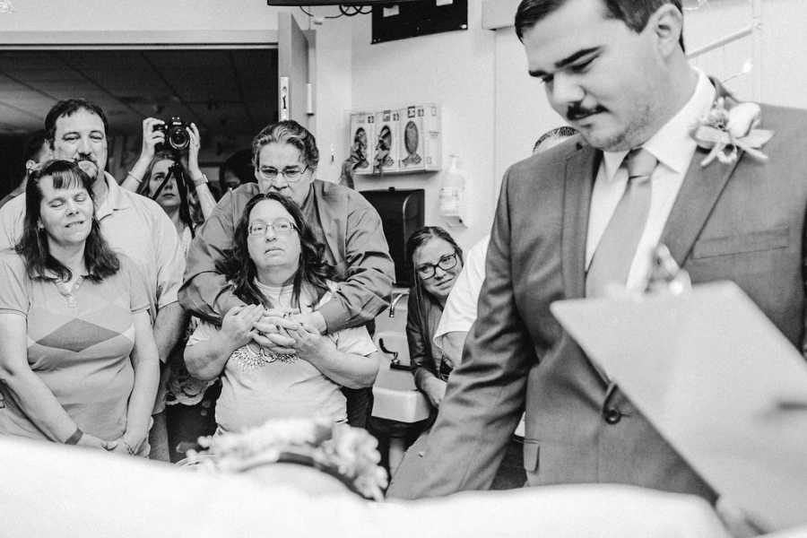 Teen groom looks down at bride with cancer while their family members watch