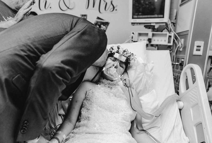 Man in suit leans over hospital bed to kiss teen bride with cancer on cheek
