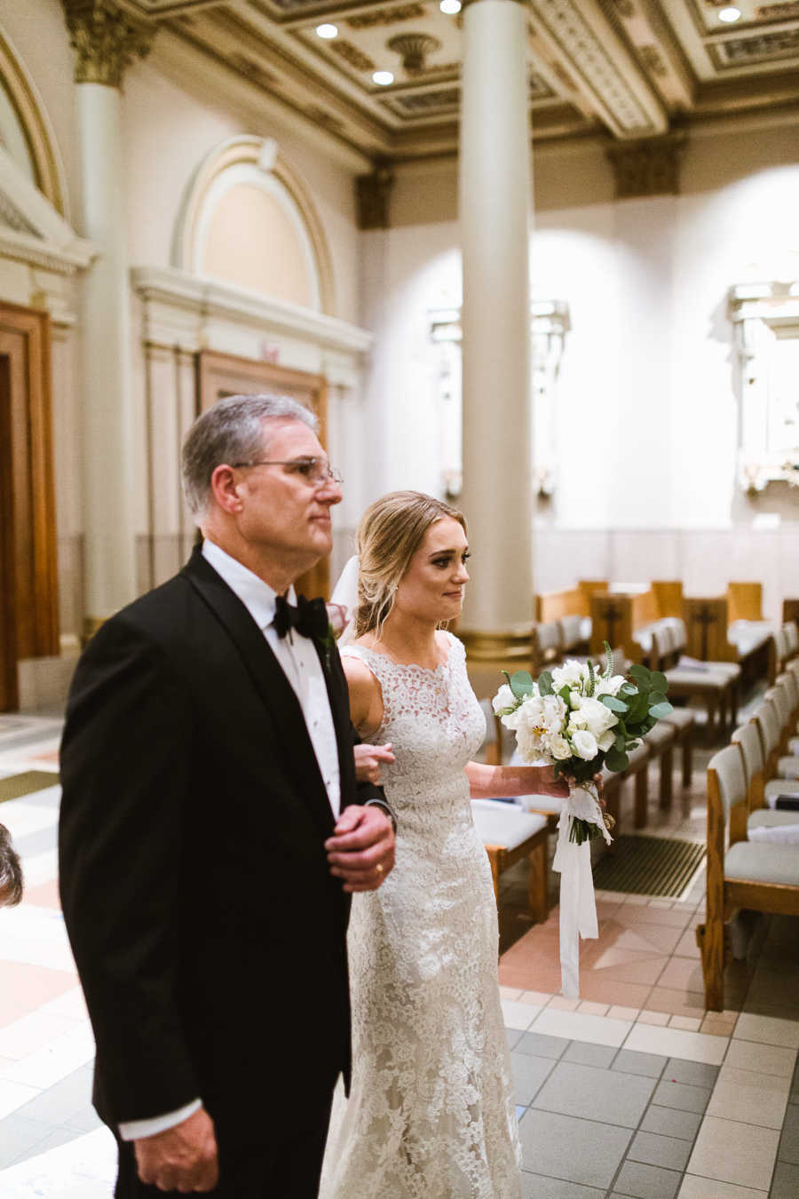 Bride and father stand arm in arm in aisle of church
