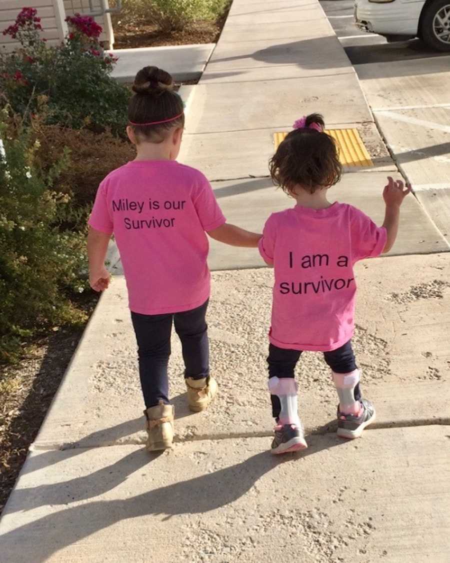 Older sister holding younger sister's hand who had shaken baby syndrome while they walk on sidewalk
