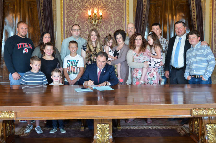 Young girl who was abused is accompanied by her family as they stand behind state representative signing bill