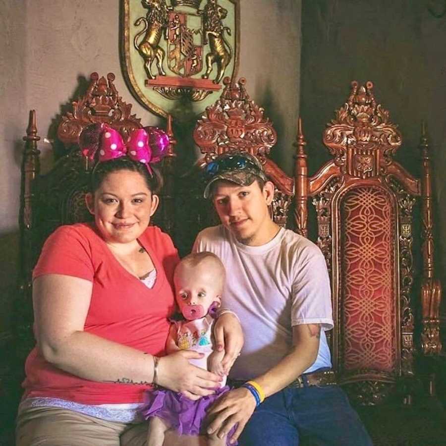 Mother and father sit with daughter in their lap who has terminal brain cancer