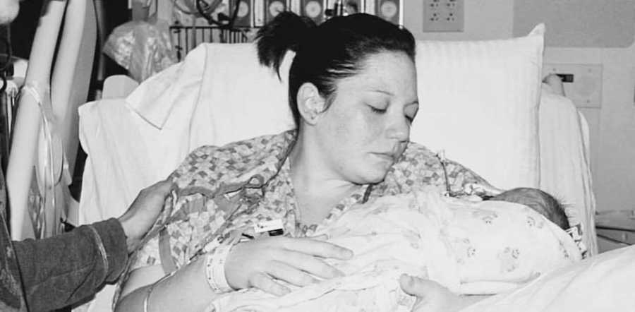 Woman sits in hospital bed looking down at newborn in her arms