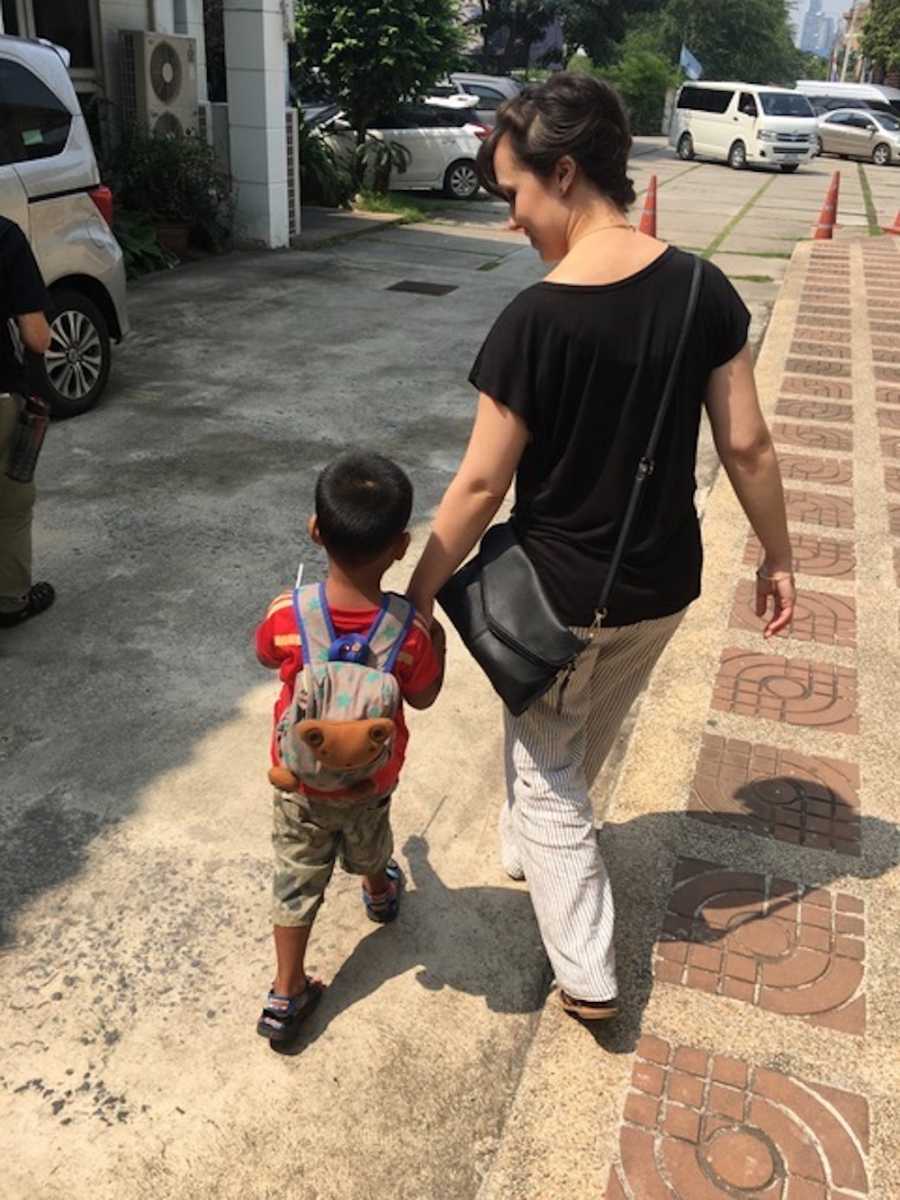 Mother holding hands with adopted toddler as they walk in parking lot