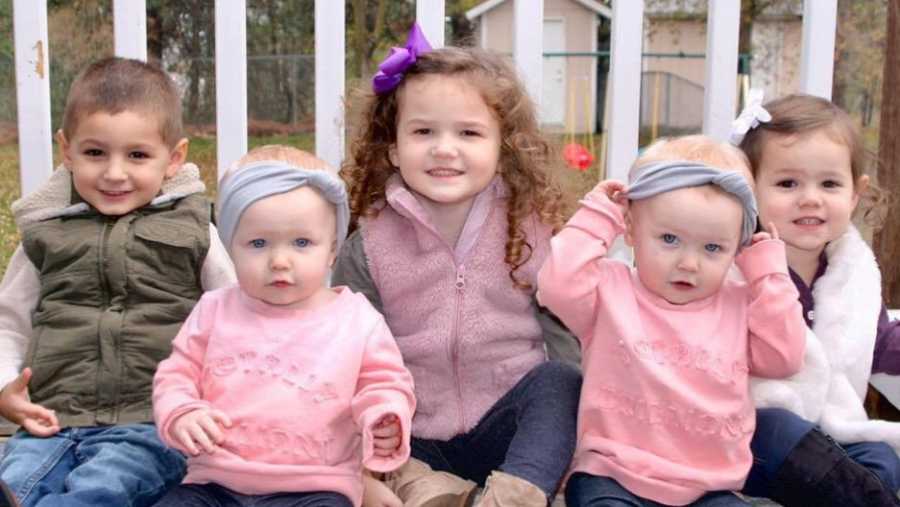 Five children sitting in a row whose mother always get's told, "You must have your hands full"