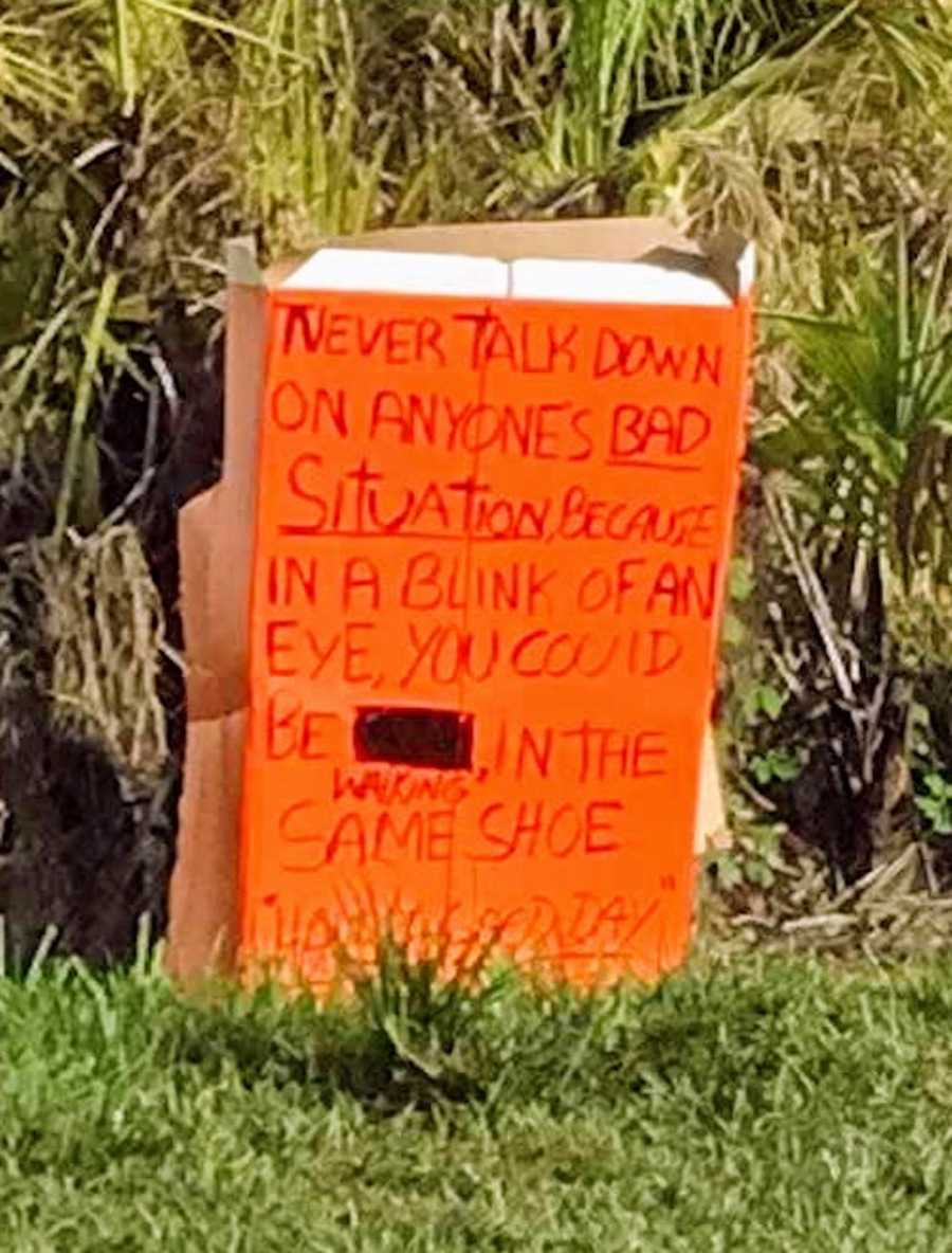 Orange sign in grass that says, "Never talk down on anyones bad situation..."