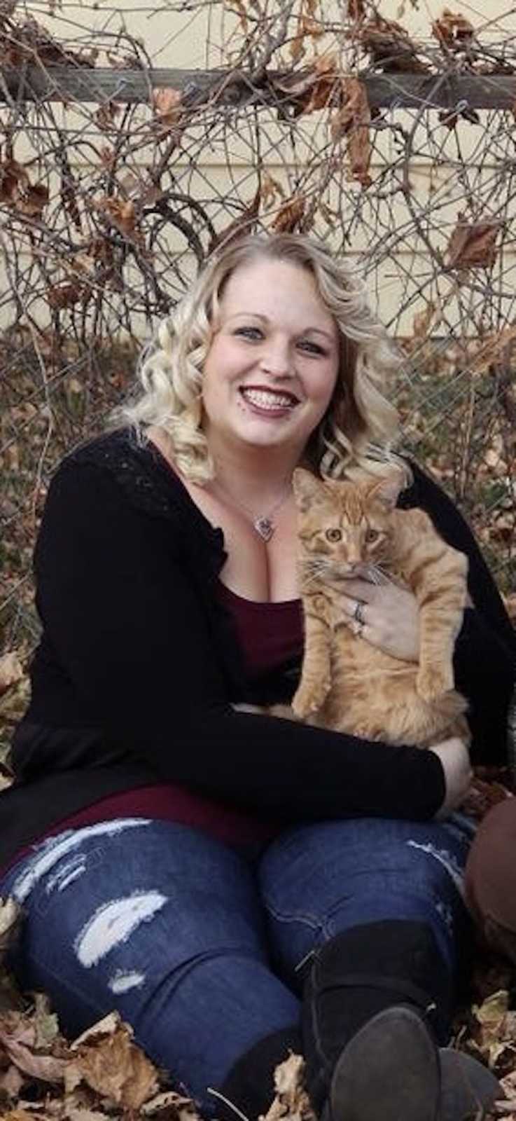 Woman who got a tattoo to cover her scars from cutting herself sits smiling with cat in her lap