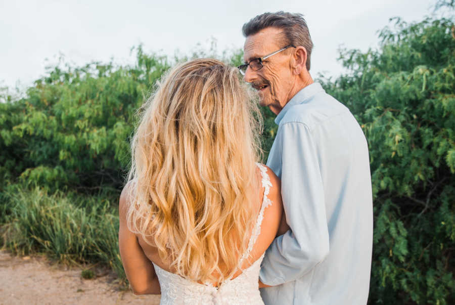 View from back of woman in wedding gown looking at her father with cancer who is smiling