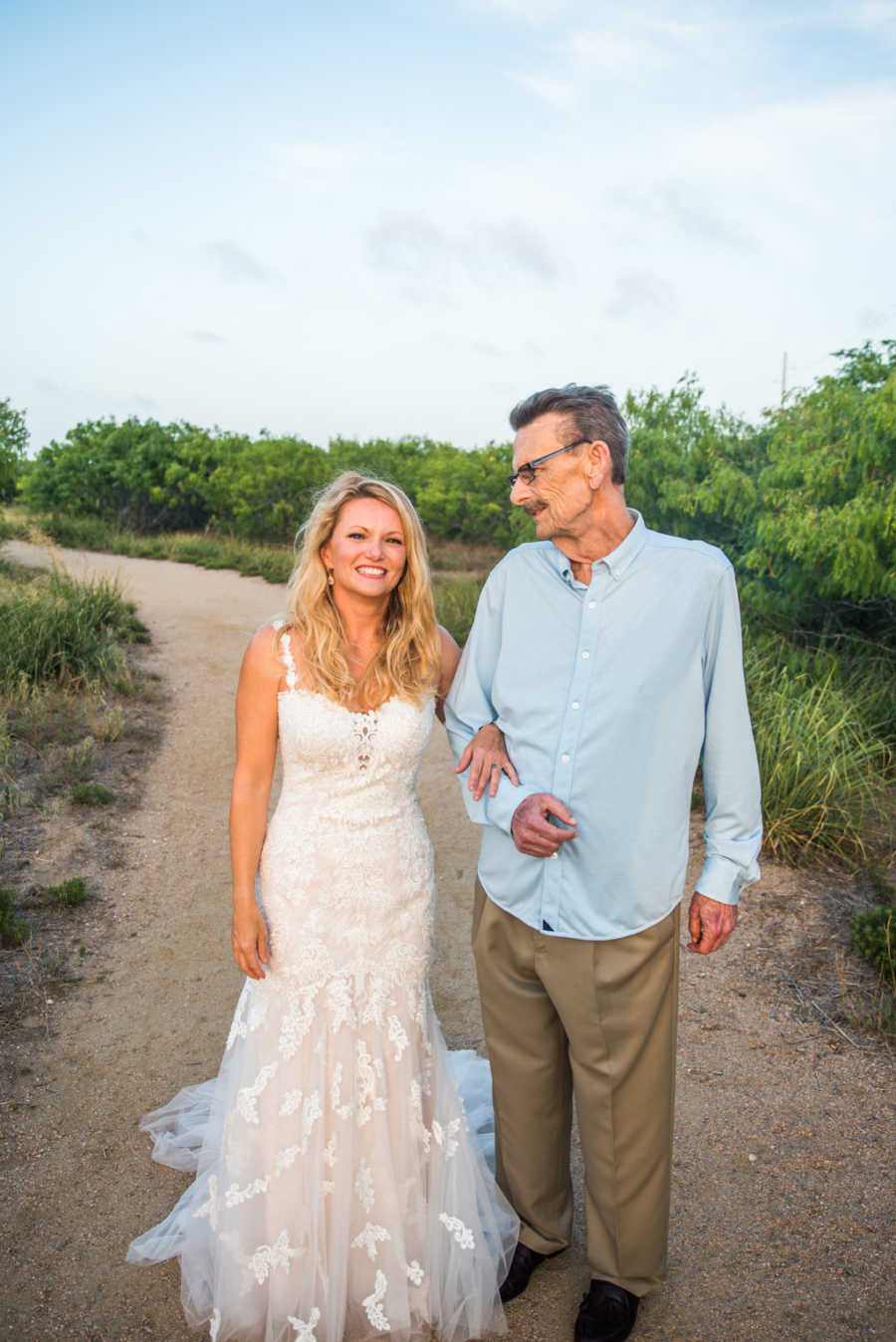 Father with cancer looks down at his daughter who is wearing a wedding dress smiling