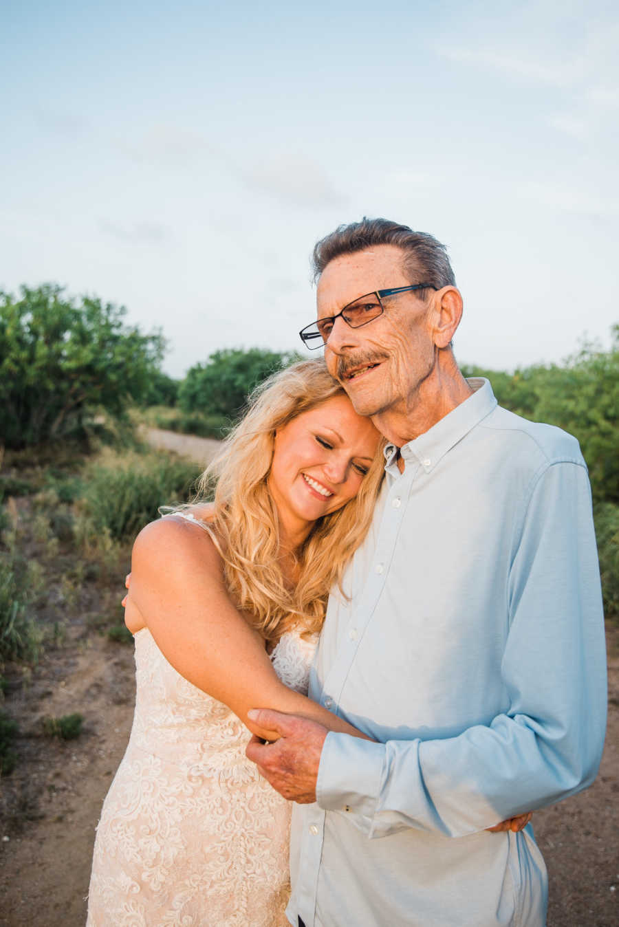 Father with cancer smiles as he holds daughter onto daughter in her wedding gown